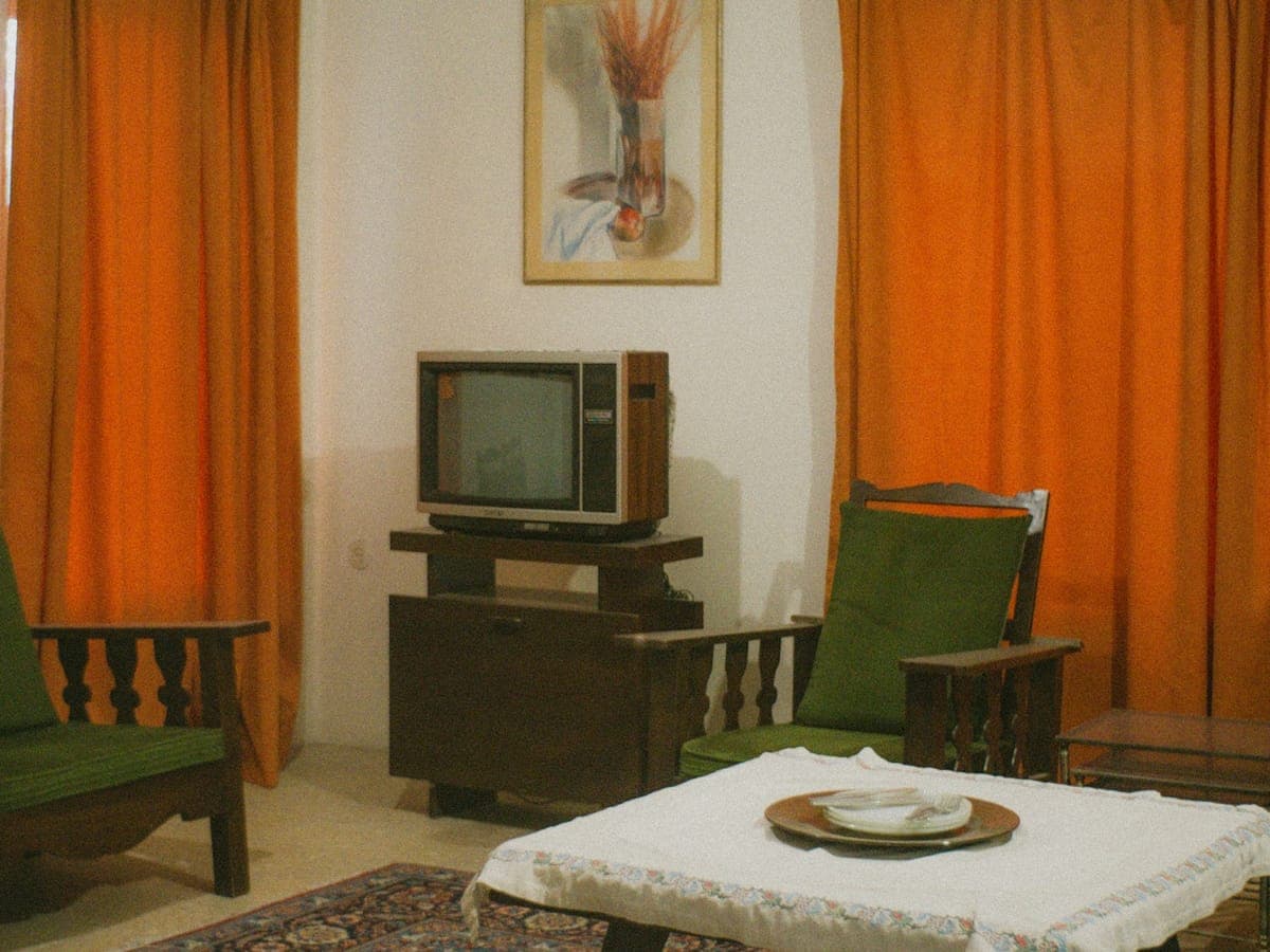 Altes Wohnzimmer mit Sesseln, Röhrenfernseher und orangefarbenen Vorhängen