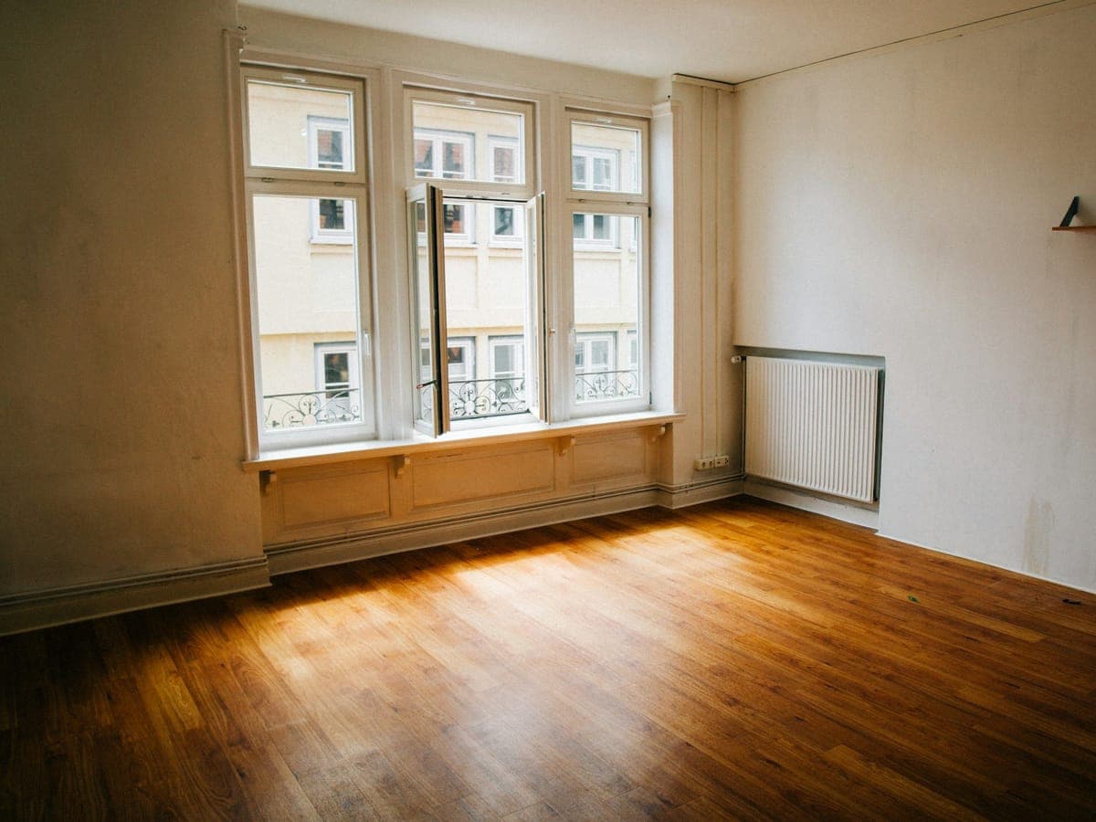 Leeres, sonniges Zimmer mit Holzboden und großem Fenster