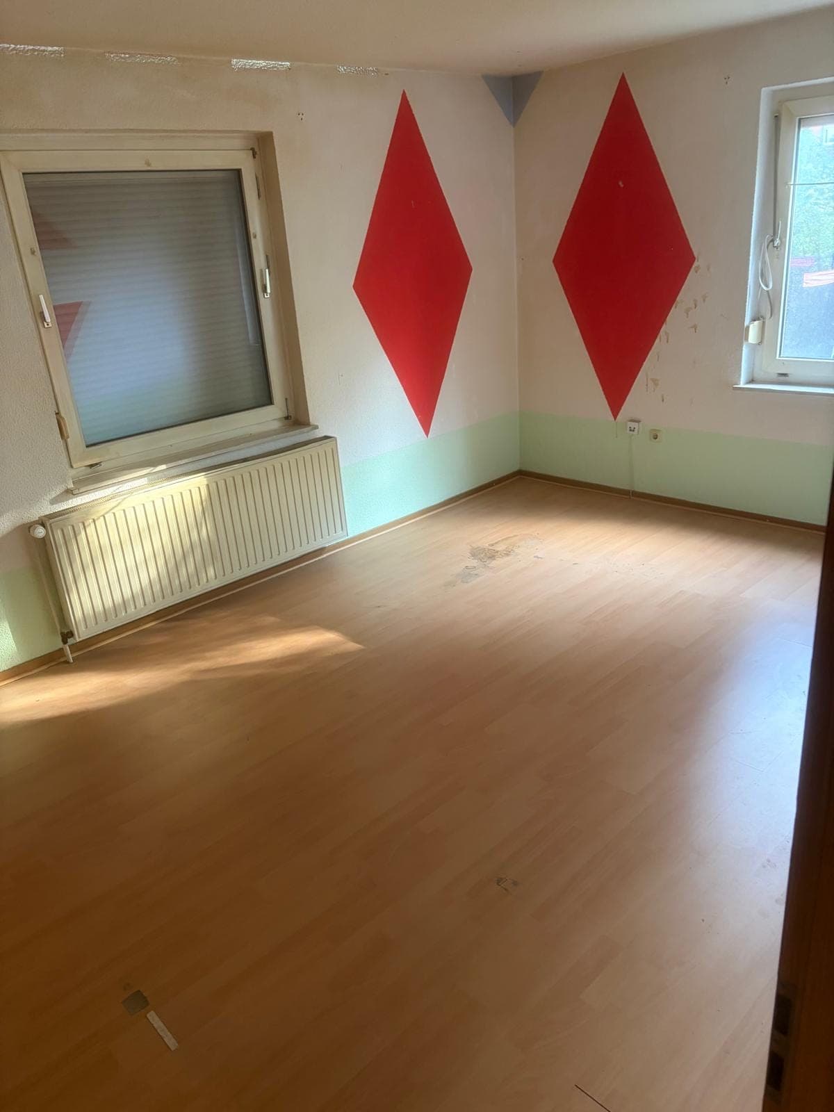 Dasselbe Wohnzimmer nach der Räumung: leer, Laminatboden gefegt, rote Rauten an der Wand